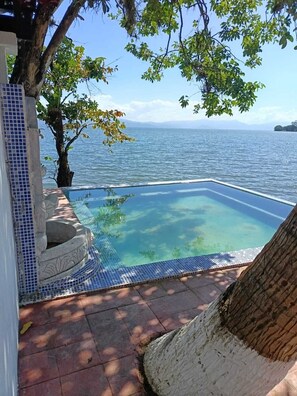 A clear blue swimming pool with a tiled edge, surrounded by a tiled patio area with a stone sculpture.