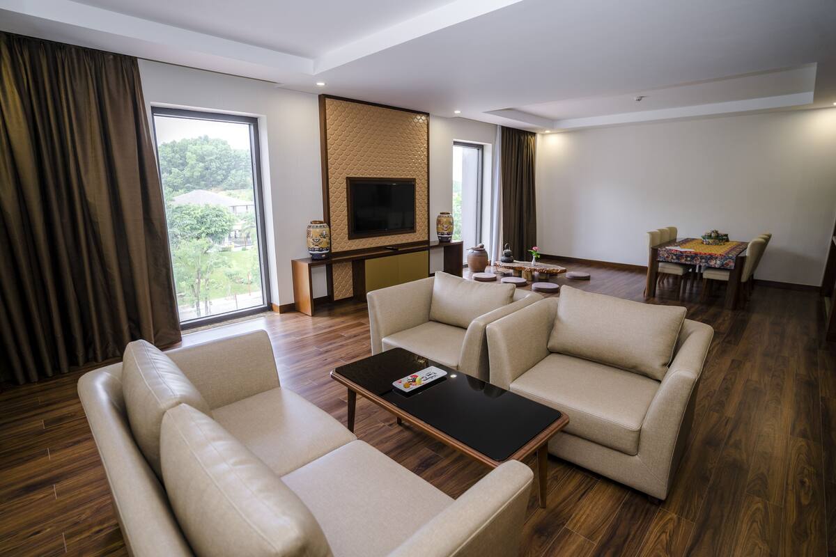 A modern living room with a sofa set, a coffee table, a TV mounted on a textured wall, and a dining area with a table and chairs.