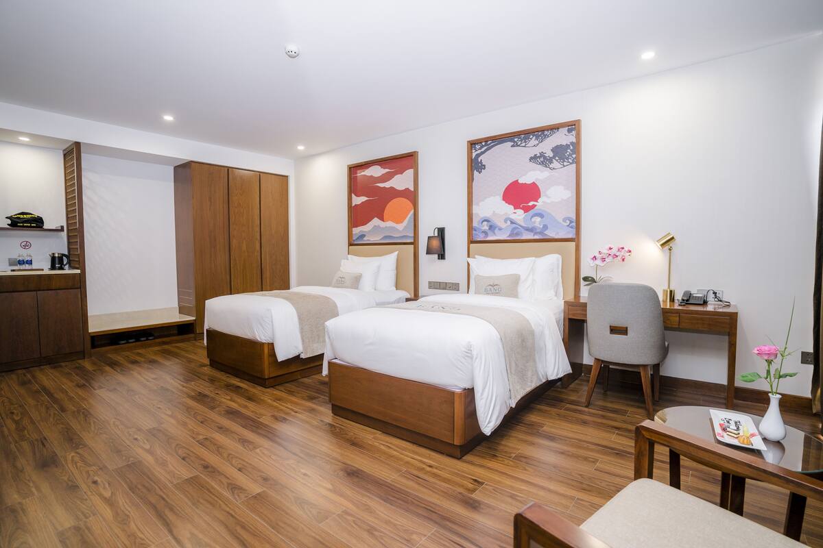 A hotel room with two beds, a desk, a chair, a small table, and artwork on the walls.