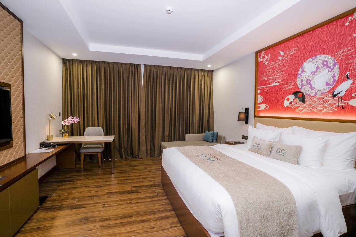 A hotel room with a bed, a desk with a chair, a television, and a large decorative wall piece.
