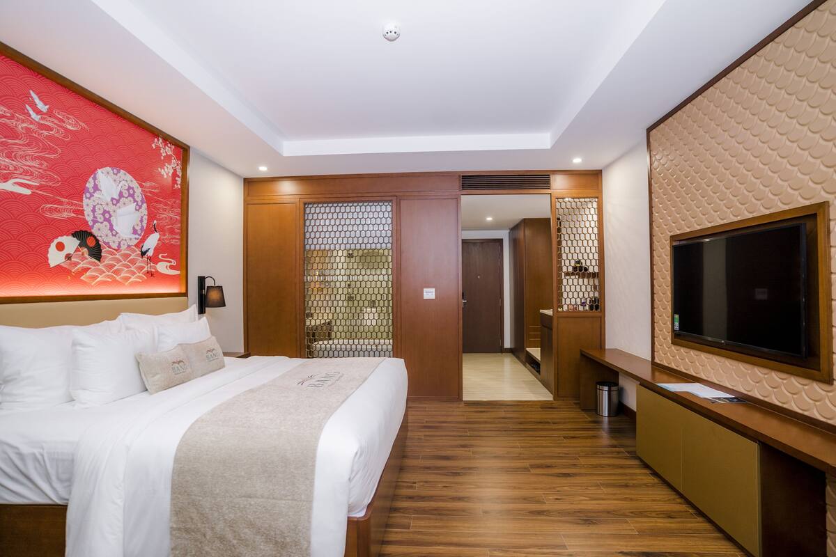 A hotel room with a bed, a TV, a wooden floor, and a decorative wall.