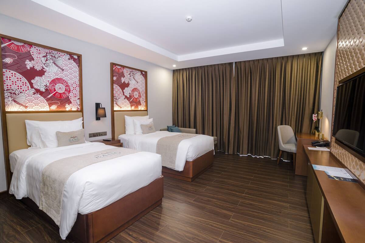 A hotel room with two beds, a desk, and a large window with curtains.