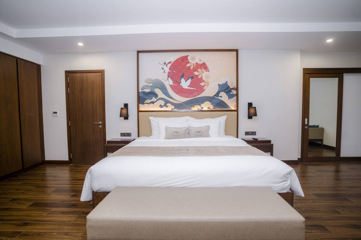 A hotel room with a large bed, wooden flooring, a wall-mounted artwork, and a door leading to another room.