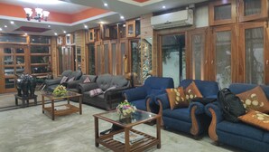 A living room with a blue sofa set, a glass coffee table, and wooden cabinets. - Hotel Sanjivani Heritage (Dibrugarh)