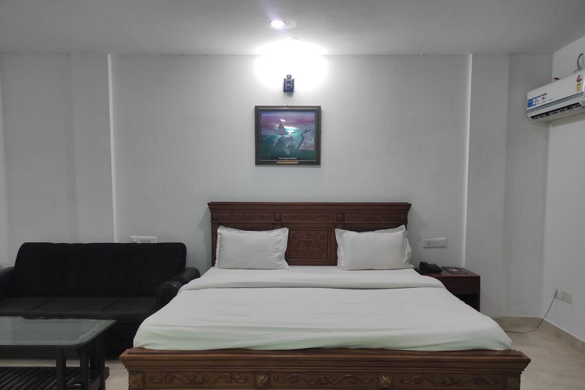 Habitación de hotel con una cama de madera, un sofá negro, una mesita y un cuadro en la pared.