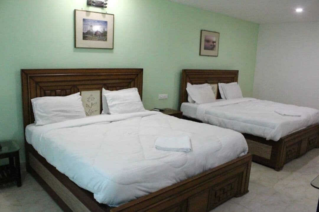 A hotel room with two single beds, each with a wooden headboard and white bedding.