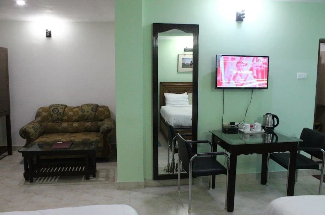 Una habitación con sofá, cama, mesa con sillas, televisor y espejo.