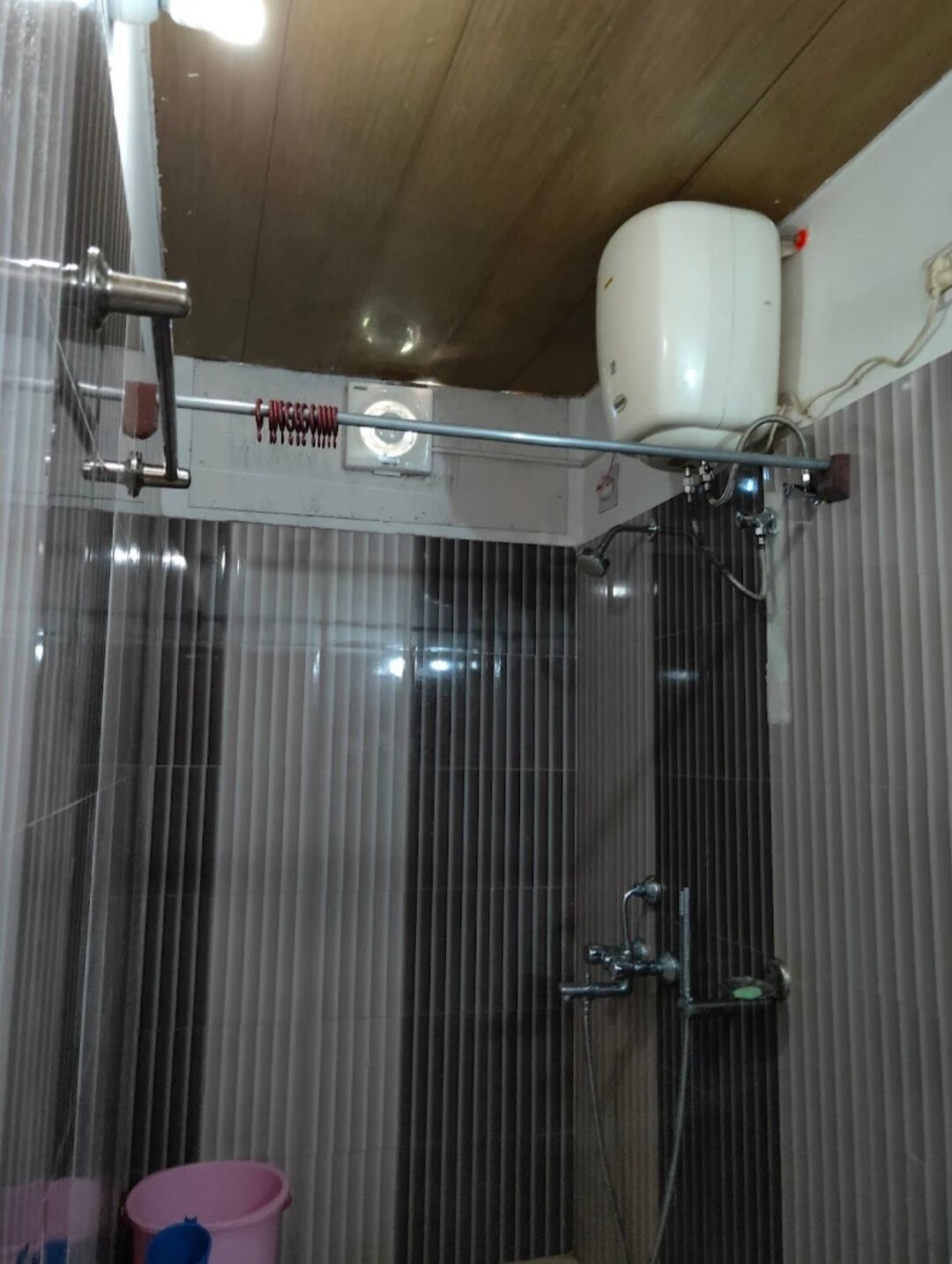 A shower area with a glass door, a white water tank, and a metal showerhead.