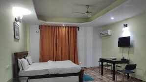 A hotel room with a bed, a desk, a chair, a TV, and an air conditioning unit. - Hotel Sanjivani Heritage (Dibrugarh)