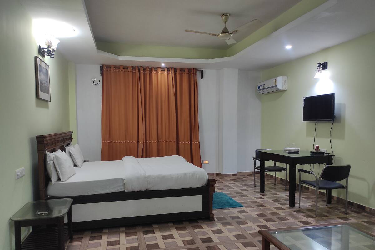 Habitación de hotel con cama, escritorio, silla, televisor y aire acondicionado.