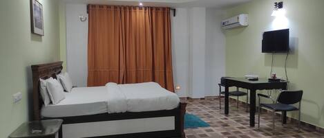Habitación de hotel con cama, escritorio, silla, televisor y aire acondicionado.