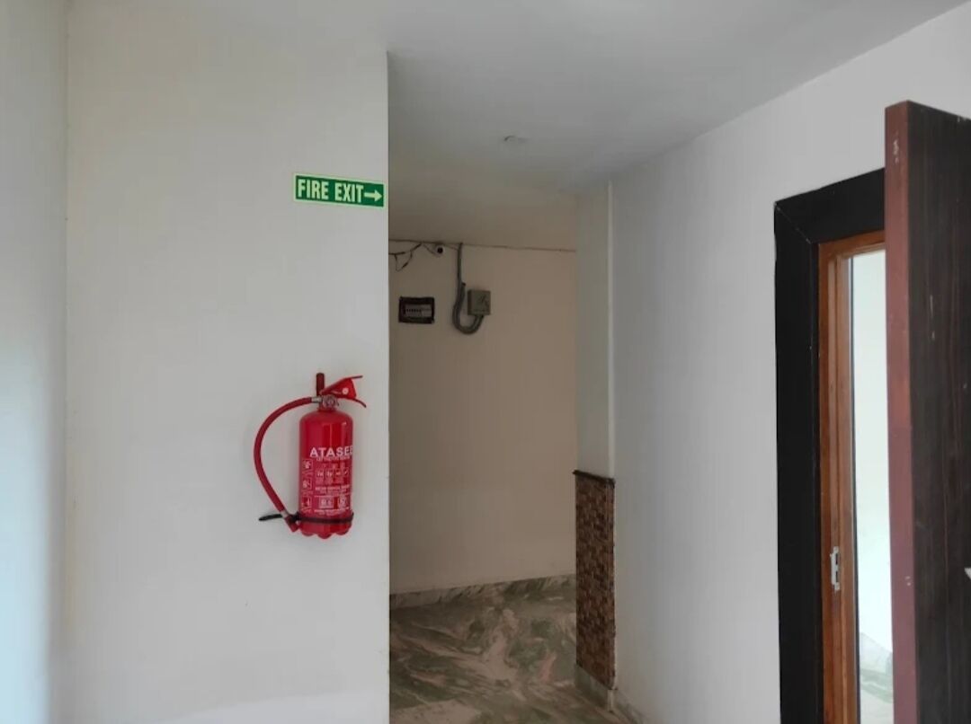 A hallway with a fire exit sign, a fire extinguisher mounted on the wall, and a door frame.