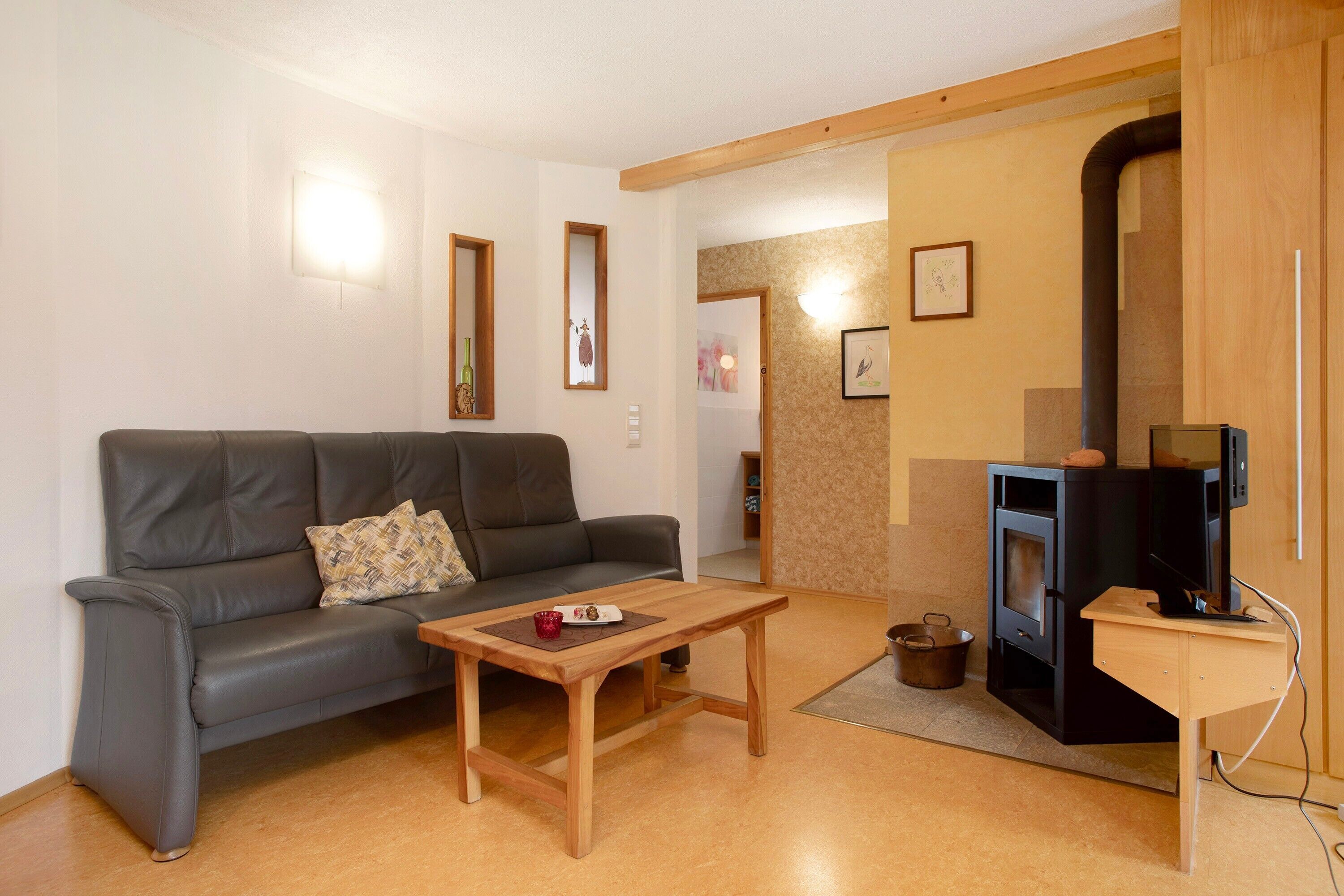 A living room with a sofa, a wooden coffee table, a television, and a wood-burning stove.