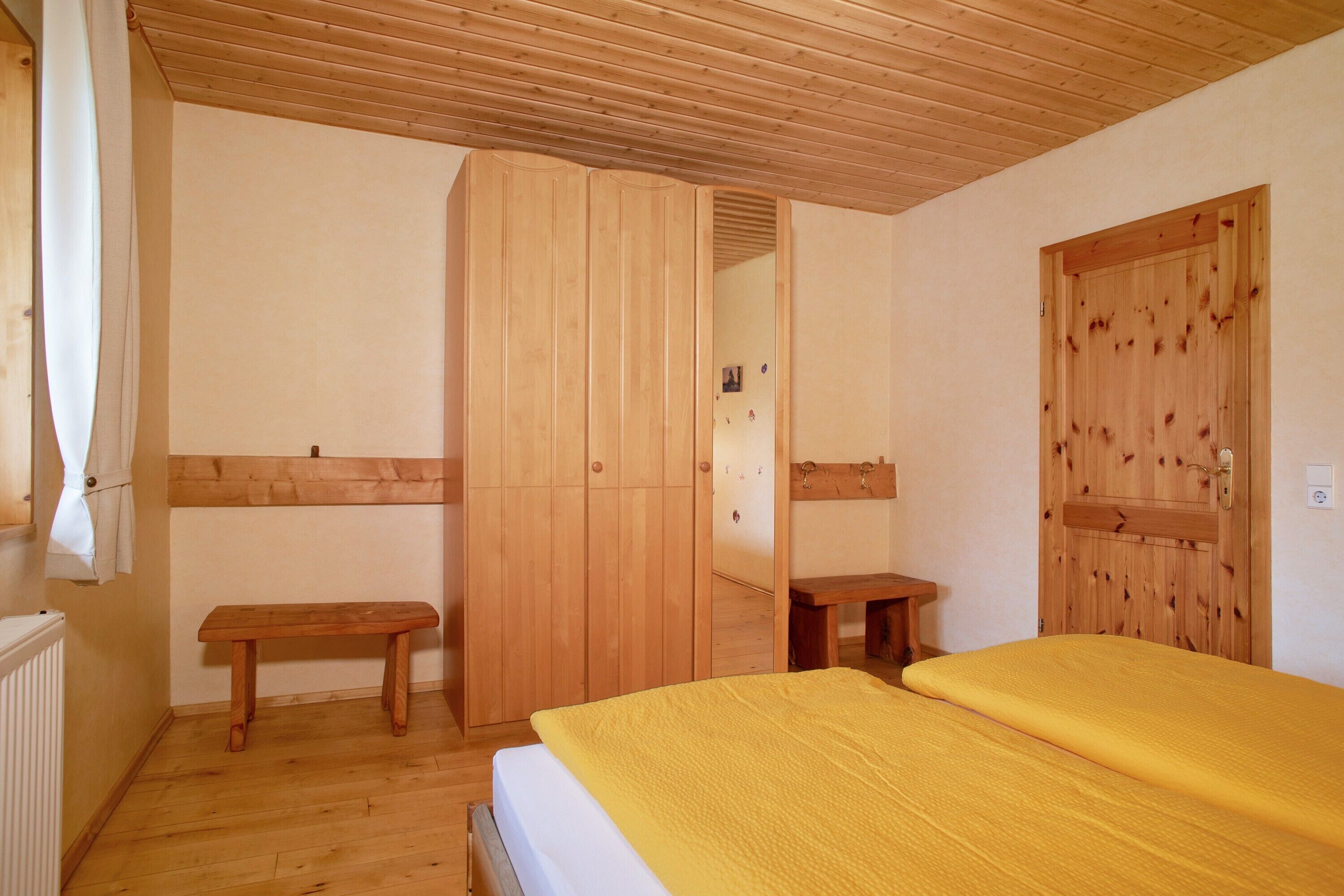 A room with a bed, a wooden bench, a wardrobe, and a door.