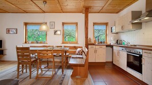 A kitchen with wooden cabinets, a dining table with chairs, a bench, and a window with a view of trees. - Apartment 'Schneckenhaus' with Shared Garden, Balcony and Wi-Fi (Ostrach- Waldbeuren)