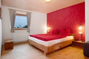 Ein Schlafzimmer mit einem hölzernen Bett, einem Fenster mit Vorhängen, einer roten Akzentwand und Nachttischlampen.