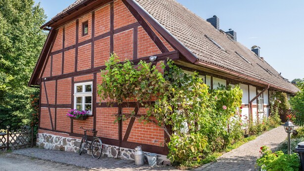 A traditional half-timbered house with a stone foundation, a bicycle, and a flower box. - Holiday Apartment 'Fachwerkferienhaus' with Lake View, Terrace & Wi-Fi (Ulrichshusen)