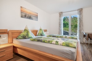 A bedroom with a bed, wooden headboard, a painting on the wall, and a window with curtains.