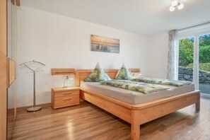 A bedroom with a wooden bed, a nightstand, a bedside table, and a floor lamp. - Vacation apartment Dandelion, 83sqm, 2 bedrooms, max. 4 persons (Ravensburg)