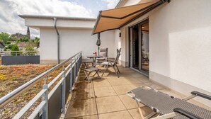 A balcony with a table, chairs, and a sunshade. - Holiday Apartment 'Im Naturpark Rhein-Westerwald' with Private Terrace and Wi-Fi (Puderbach)