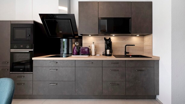 A modern kitchen with dark cabinetry, a built-in microwave, a coffee maker, and a sink. - Holiday Apartment 'Im Naturpark Rhein-Westerwald' with Private Terrace and Wi-Fi (Puderbach)