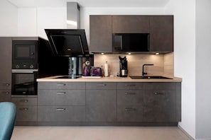 A modern kitchen with dark cabinetry, a built-in microwave, a coffee maker, and a sink.