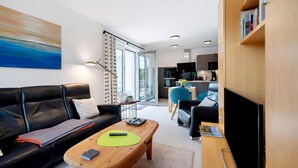 A modern living room with a black leather sofa, a wooden coffee table, a TV, and a bookshelf. - Holiday Apartment 'Im Naturpark Rhein-Westerwald' with Private Terrace and Wi-Fi (Puderbach)
