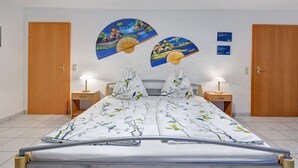 Ein Bett mit weißer Blumenbettdecke, zwei Nachttische mit Lampen, Holztüren und ein an der Wand befestigtes Kunstwerk.