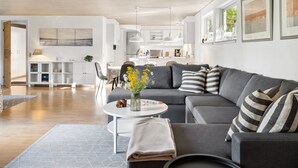 A modern living room with a grey sofa, a round coffee table, and a dining area in the background.