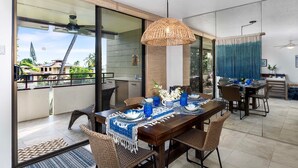 Un coin repas avec une grande table dressée pour quatre personnes, entourée de chaises en osier, et donnant sur le balcon extérieur.