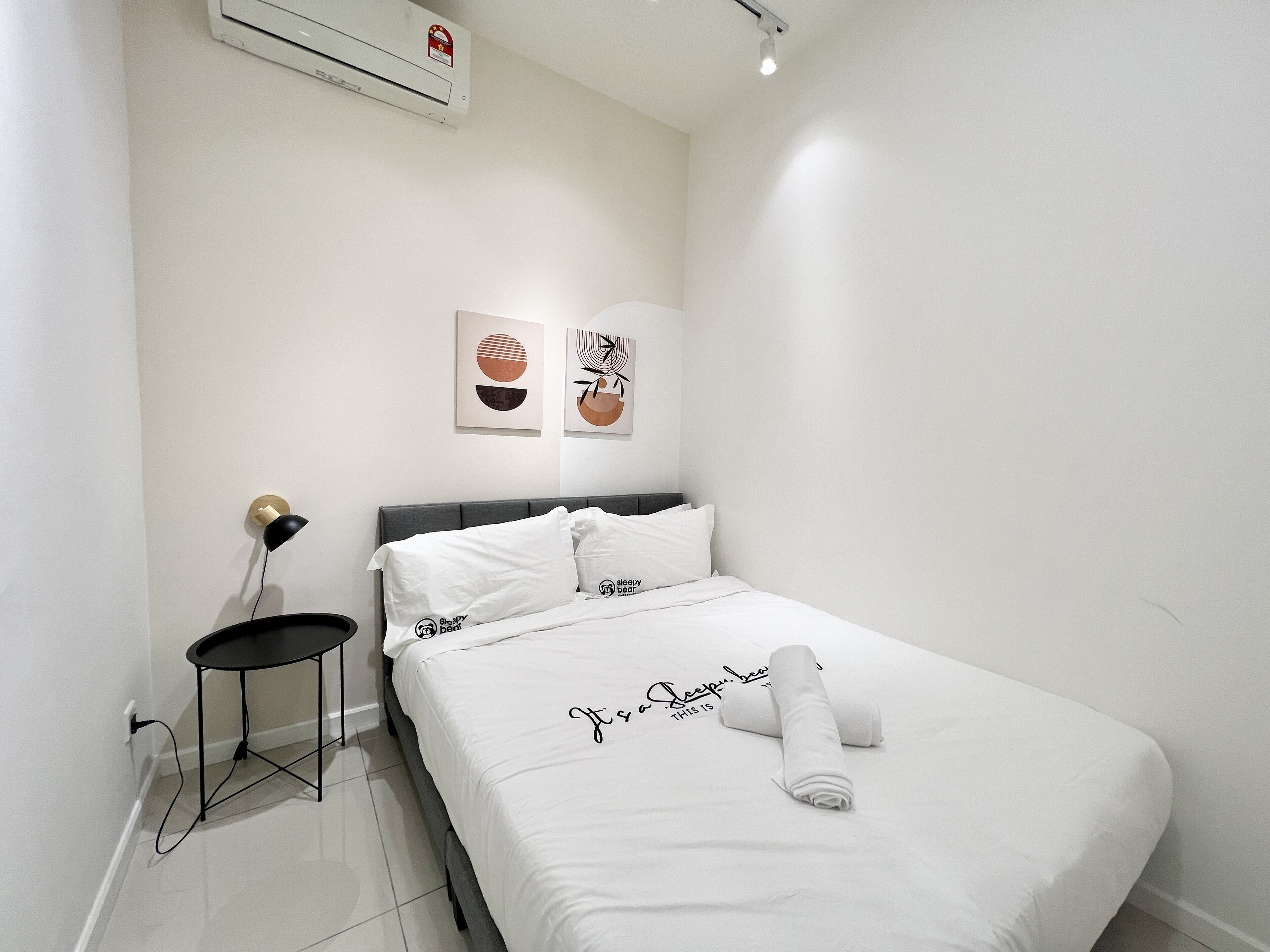 A neatly made bed with a towel, a small bedside table, and wall art.