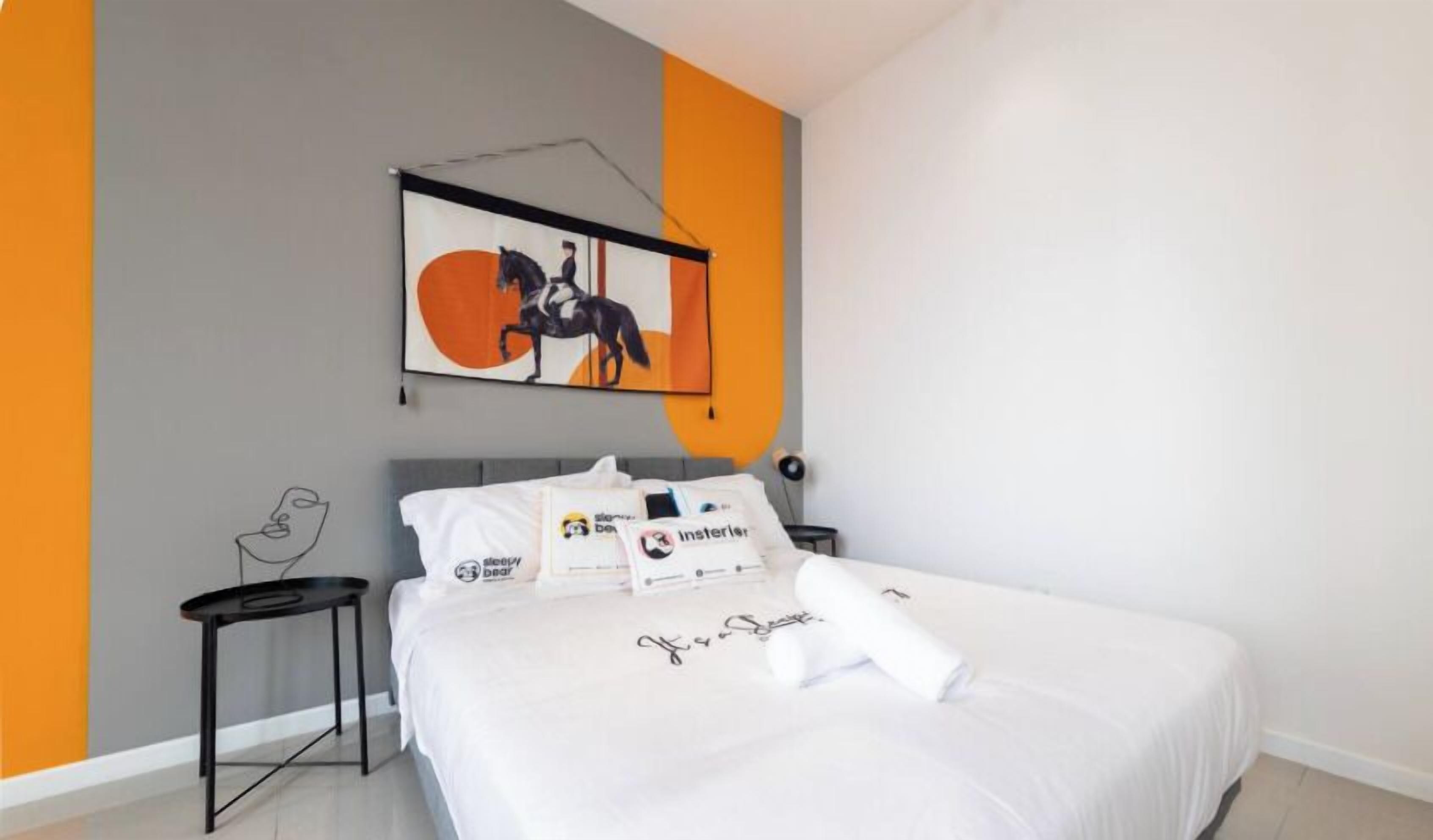 A neatly made bed with white linens and pillows, a small bedside table, a wall-mounted artwork of a horse, and a partial view of a room with orange and grey walls.