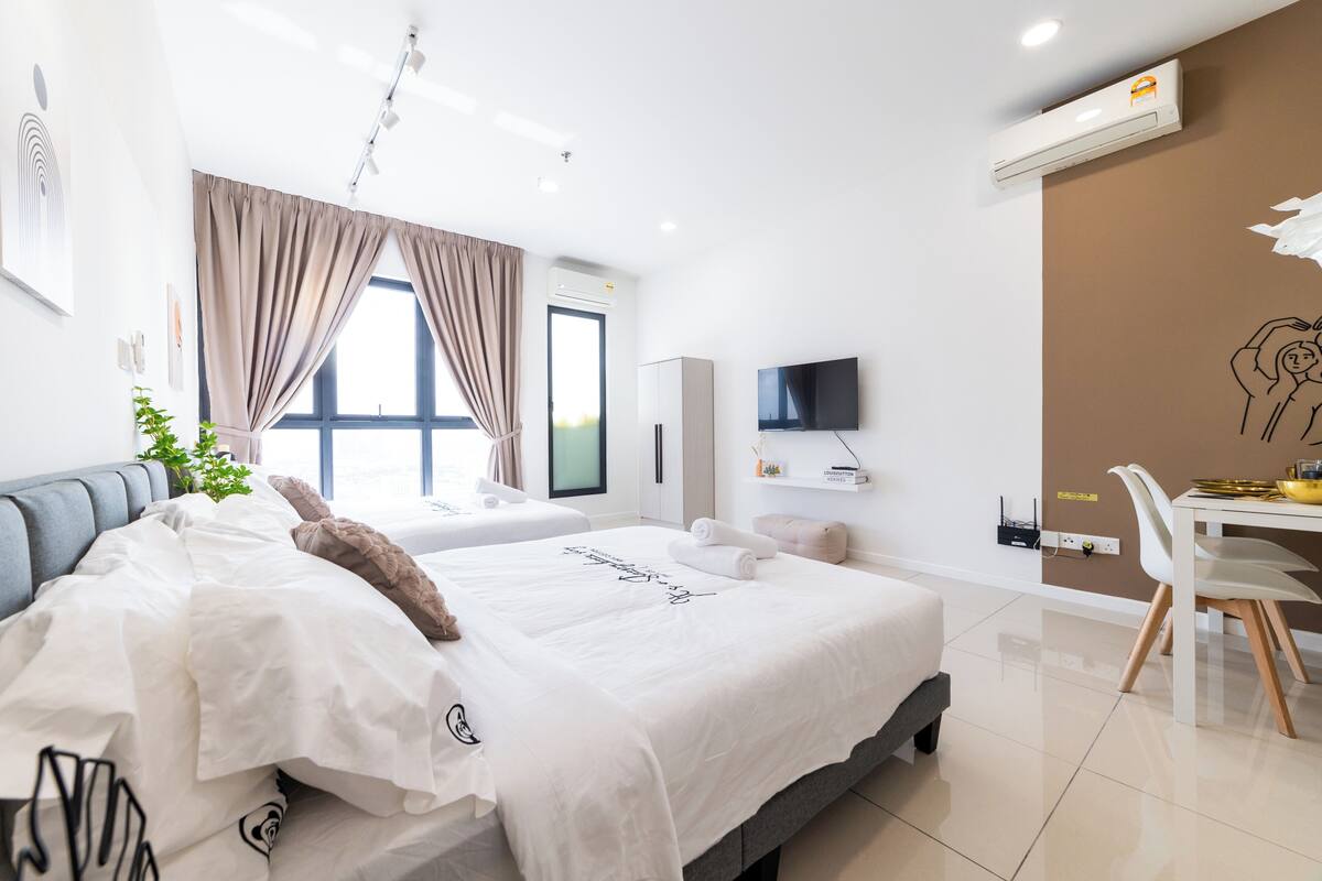 A modern hotel room with a large bed, a desk, a flat-screen TV, and a dining area.