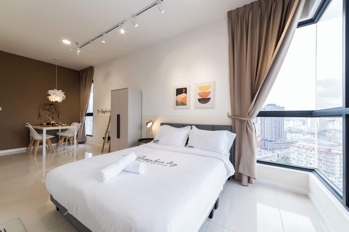 A modern hotel room with a large bed, a dining area, and a city view.