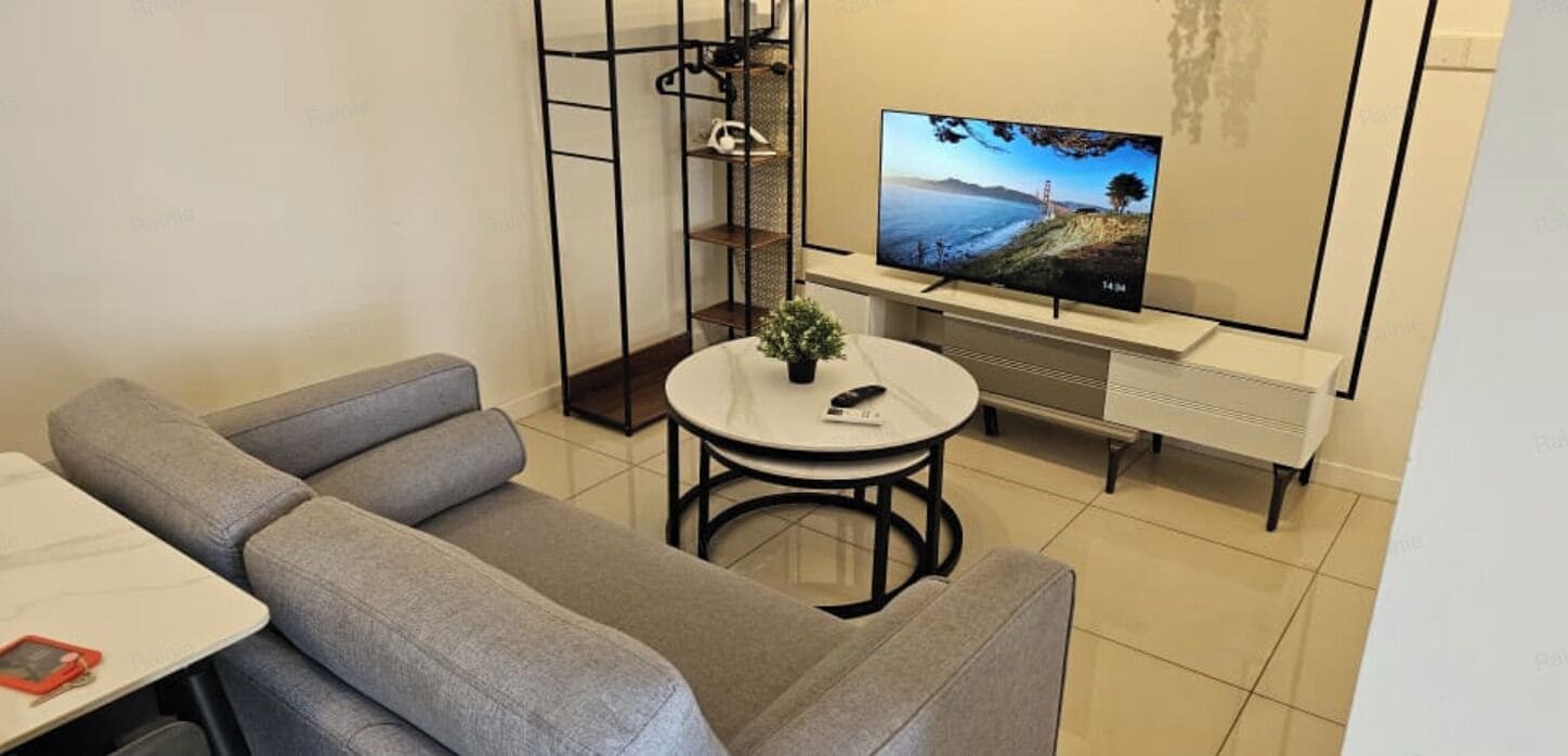 A modern living room with a grey sofa, a small round table with a plant, a TV on a stand, and a metal shelving unit.