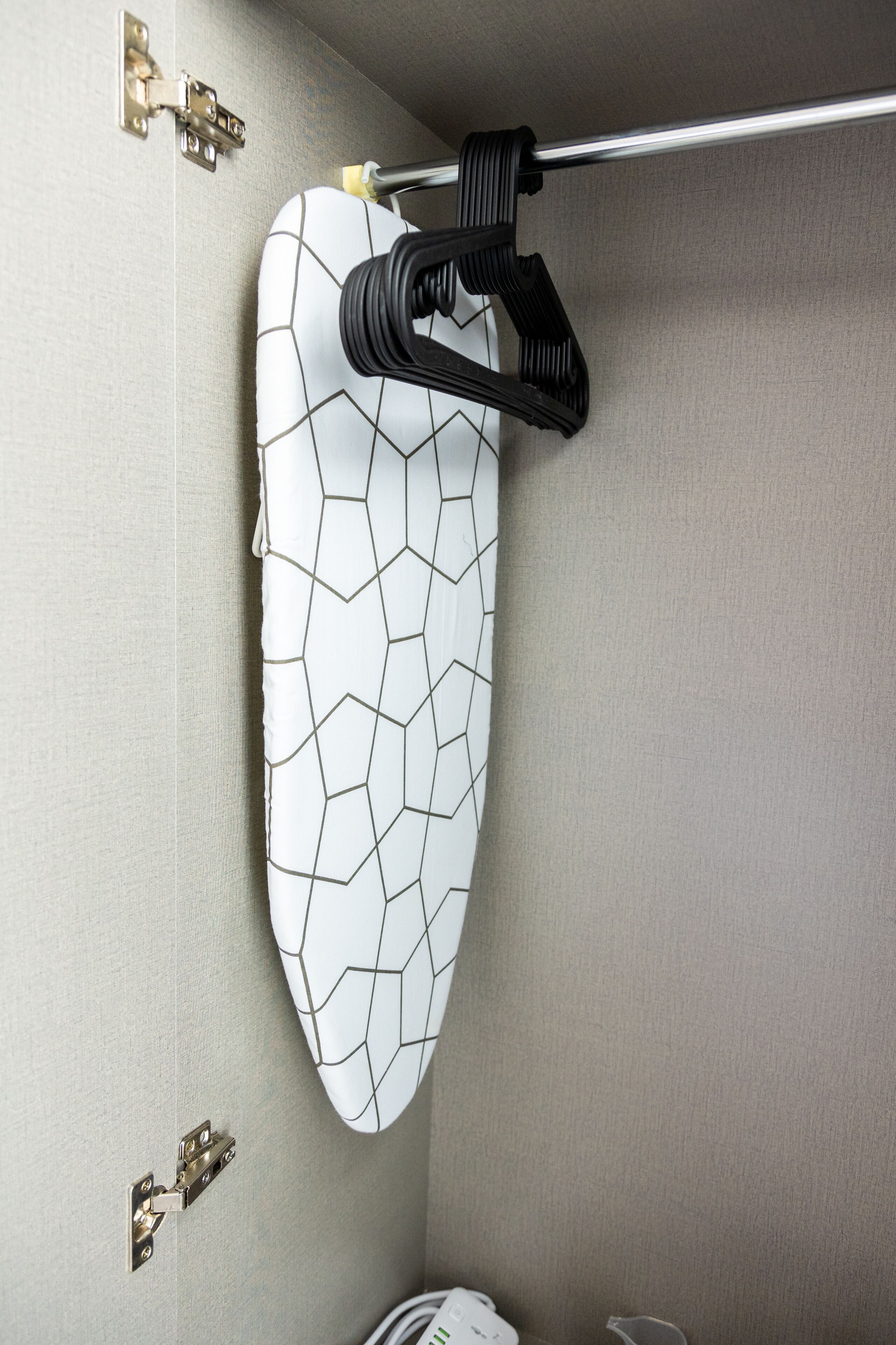 Ein an der Wand befestigtes Bügelbrett mit geometrischem Muster, einem Metallhaken und einer Kabelaufwicklung.