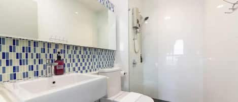 Un baño moderno con lavamanos blanco, inodoro y ducha con mampara de vidrio.