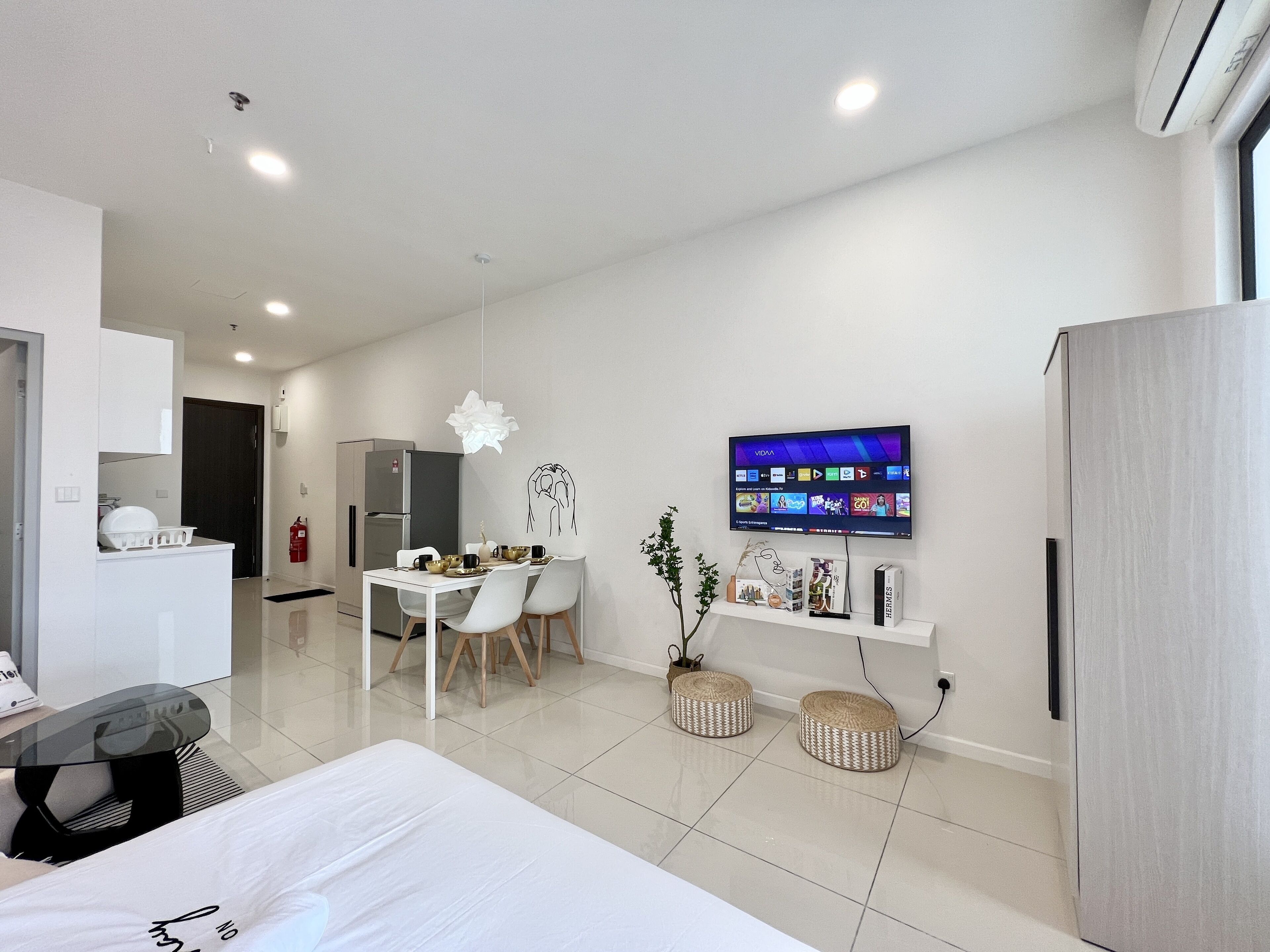 Une chambre d’hôtel moderne équipée d’un lit, d’un coin repas avec des chaises et une table, d’un téléviseur fixé au mur et d’un réfrigérateur.