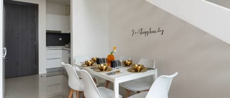 A modern dining area with a white table, four chairs, and a decorative wall with a phrase.