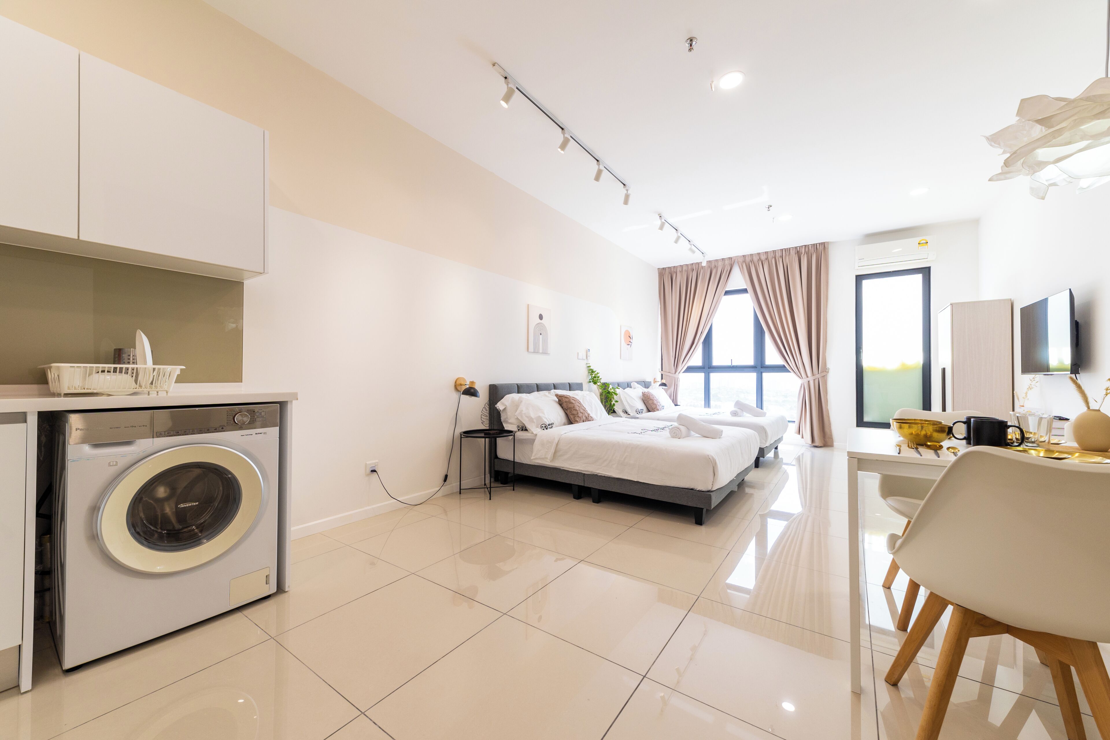 Habitación de hotel moderna con cama, lavadora, zona de comedor y un amplio ventanal.