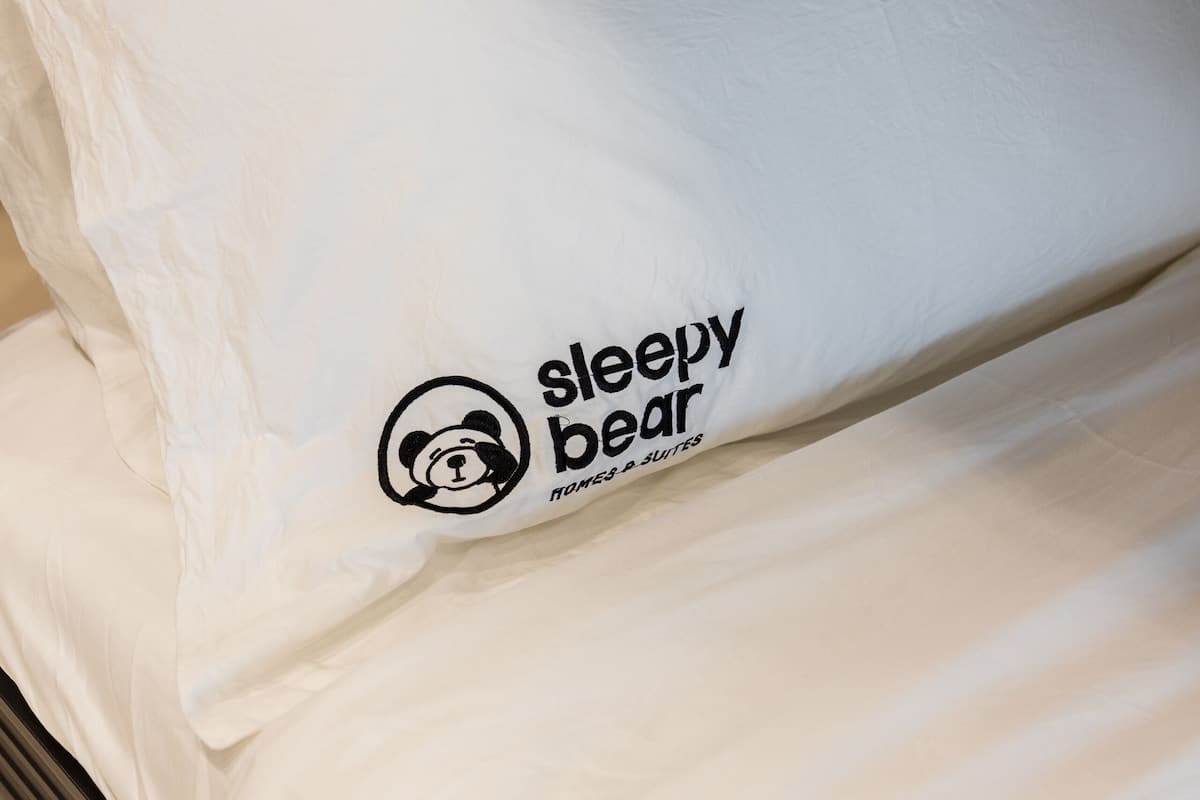 A bed with white bedding and a pillow featuring a logo and text.