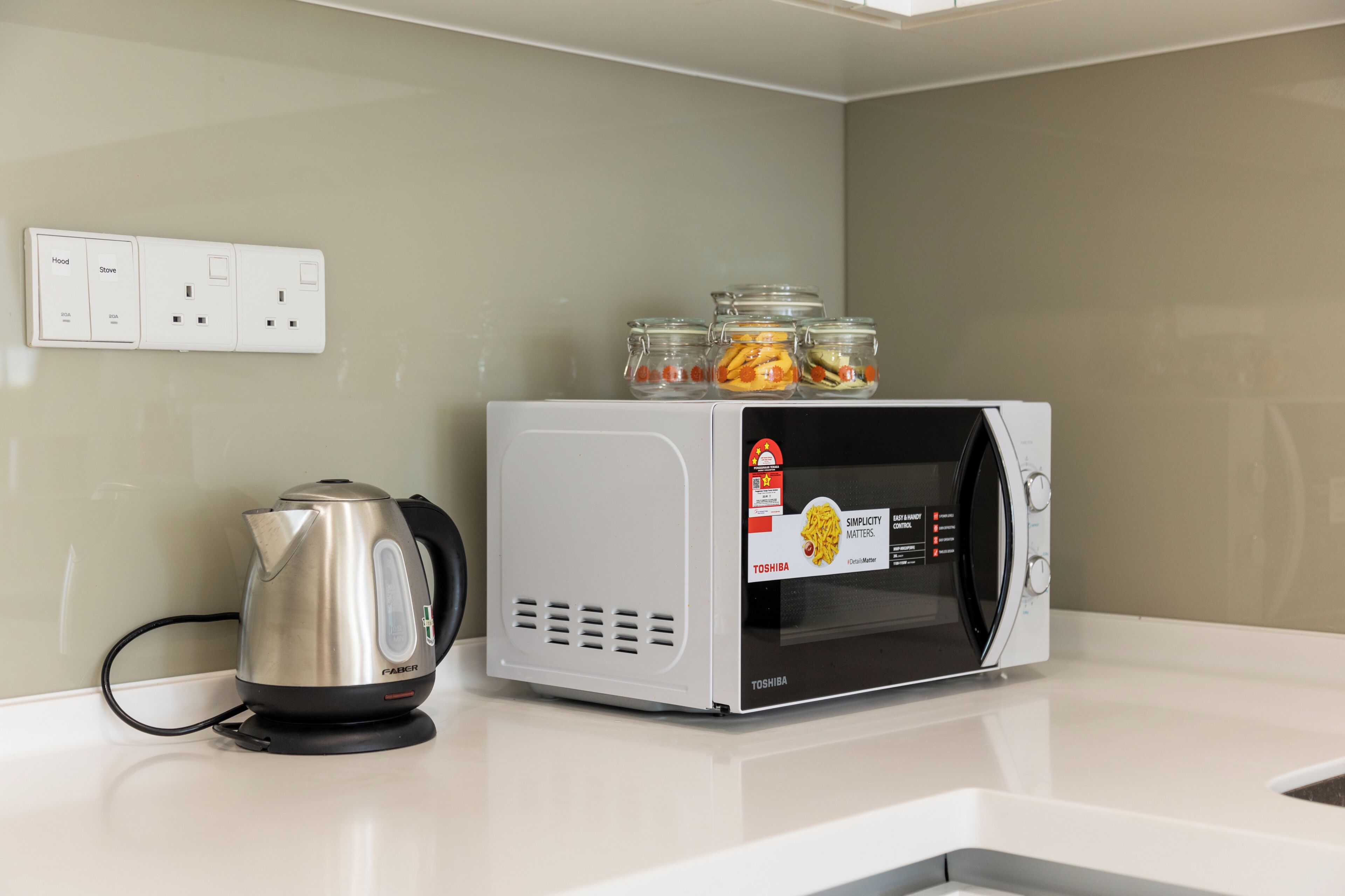 A kitchen with a kettle, a microwave, and jars of food on the counter.