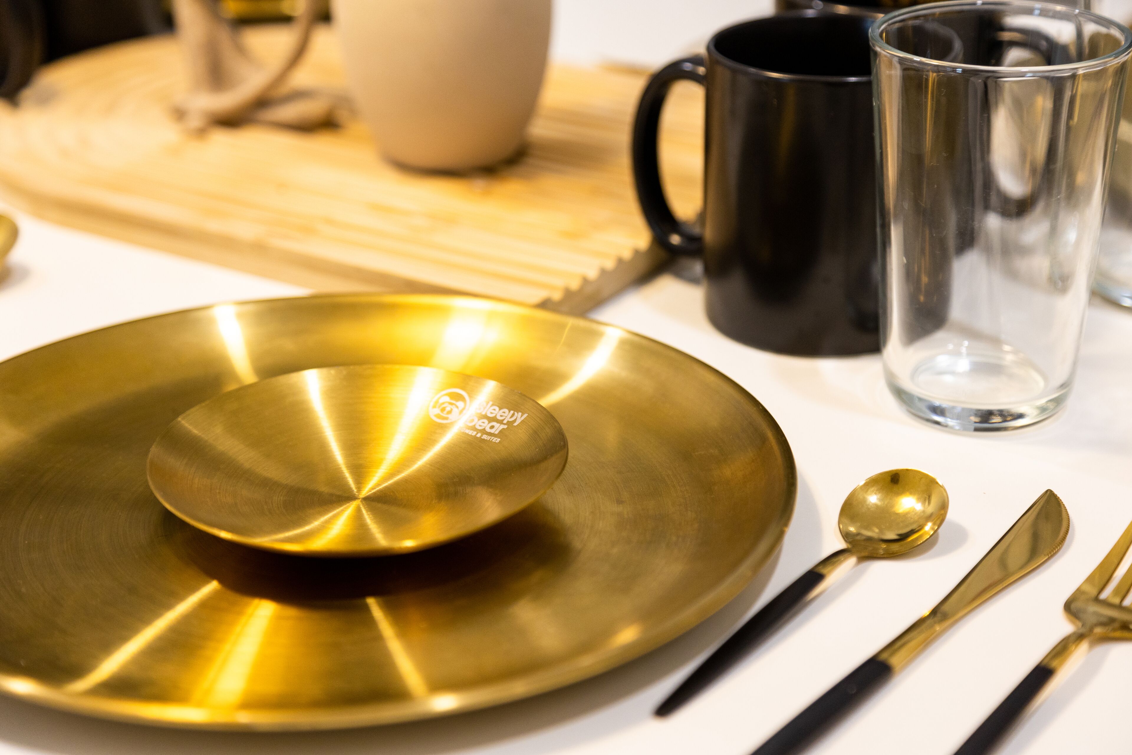 A table setting with a gold plate, a spoon, a knife, and a black mug.