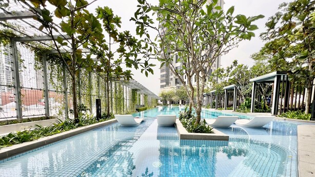 Una piscina con bordes de azulejos, rodeada de árboles y un edificio al fondo.