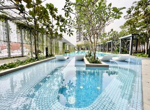 Una piscina con bordes de azulejos, rodeada de árboles y un edificio al fondo.