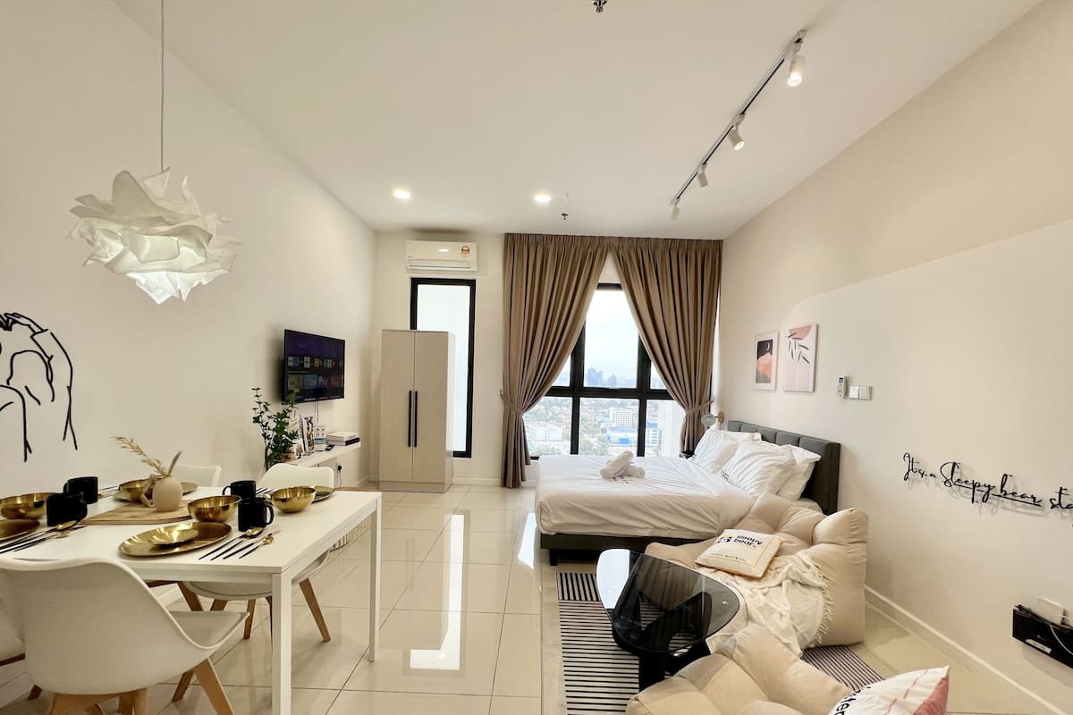 A modern hotel room with a bed, a desk, and a dining area.