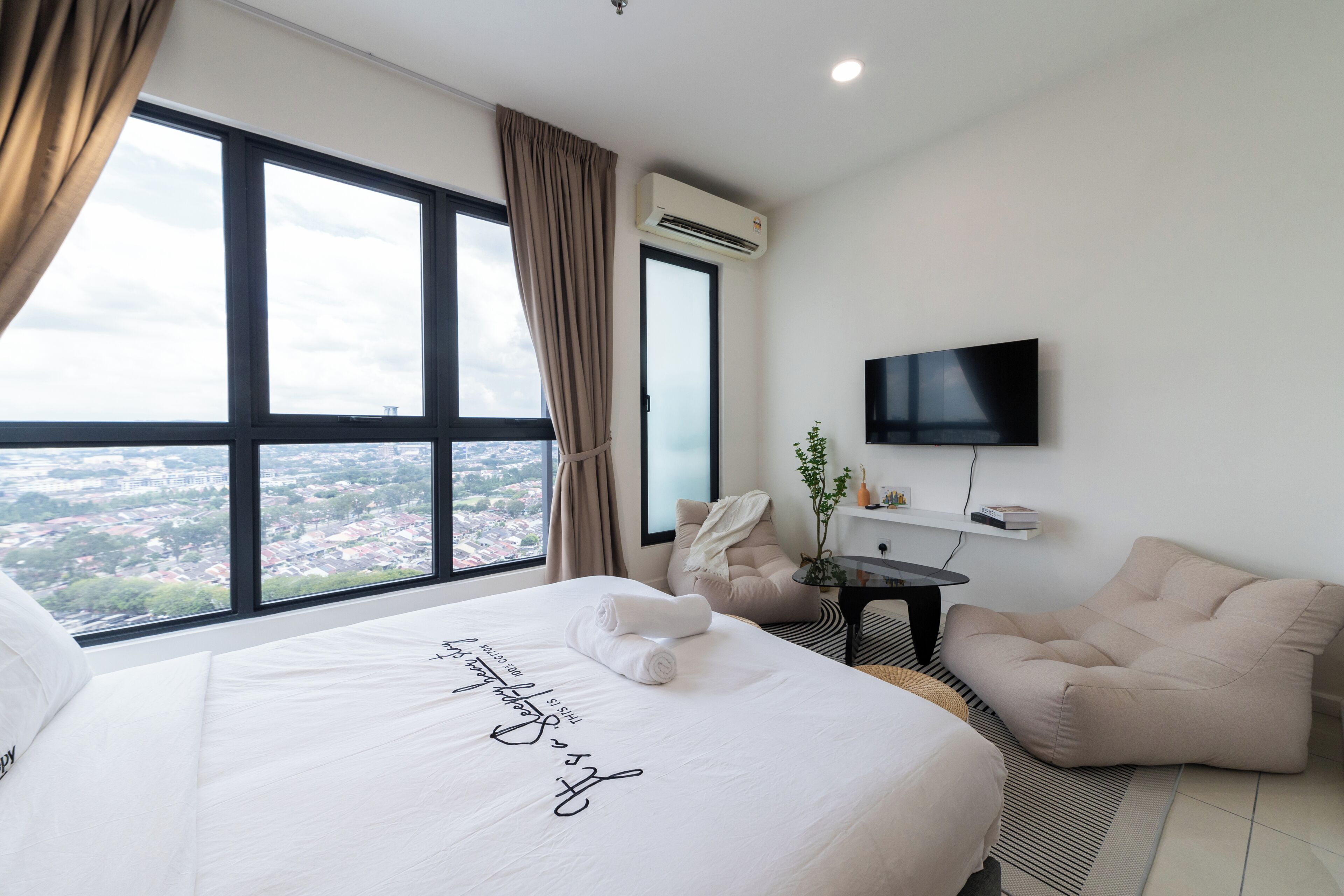 A hotel room with a large bed, a TV, a chair, and a view of the city.