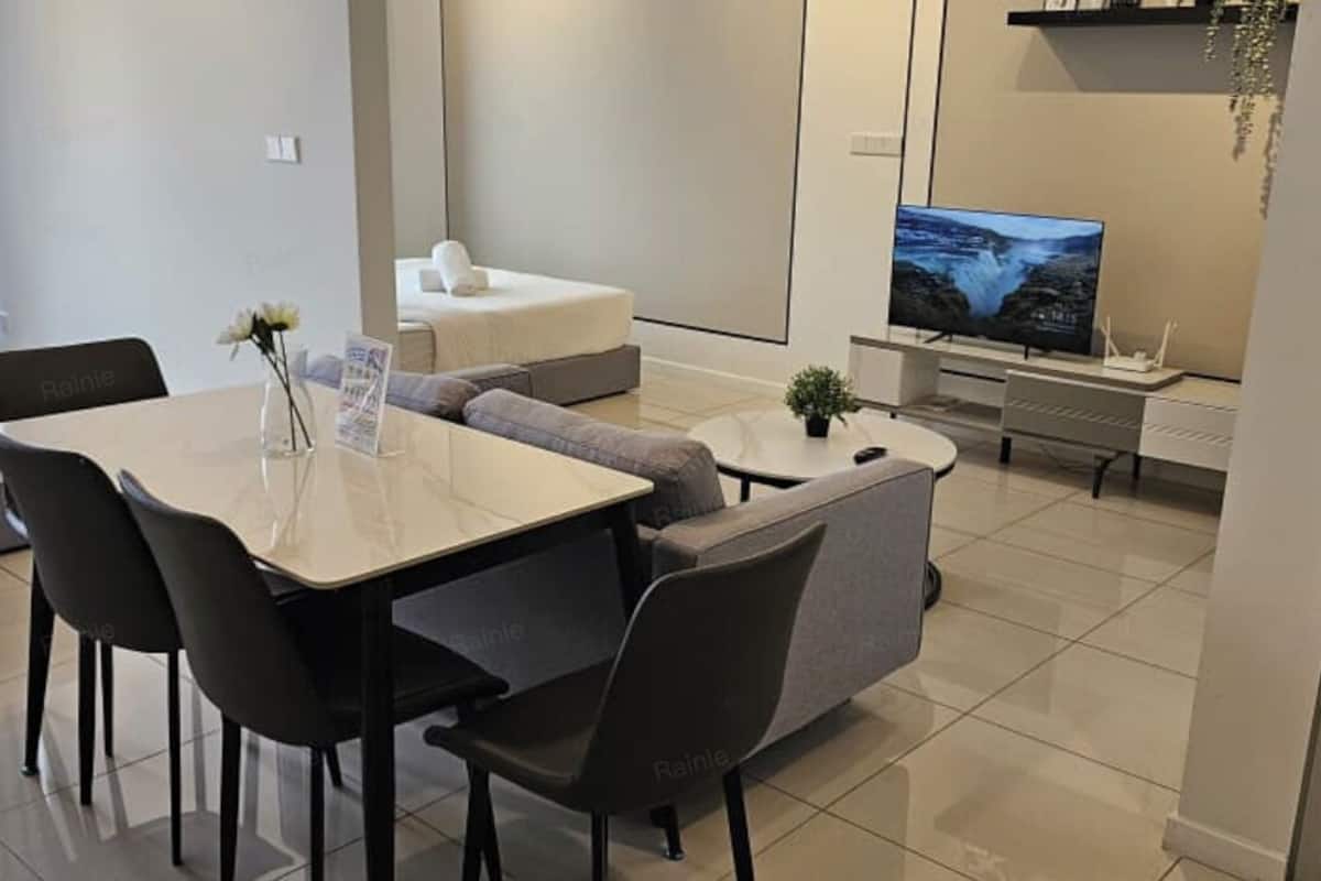 A modern hotel room with a dining area, a sofa, a TV, and a view of the city.