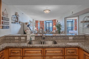 A kitchen with granite countertops, wooden cabinets, a stainless steel sink, and a view of the ocean through large windows.