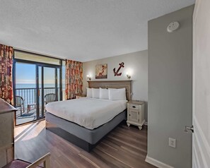 Una camera d'albergo con un letto grande, un comodino, una sedia, un balcone con tende e vista sul mare.